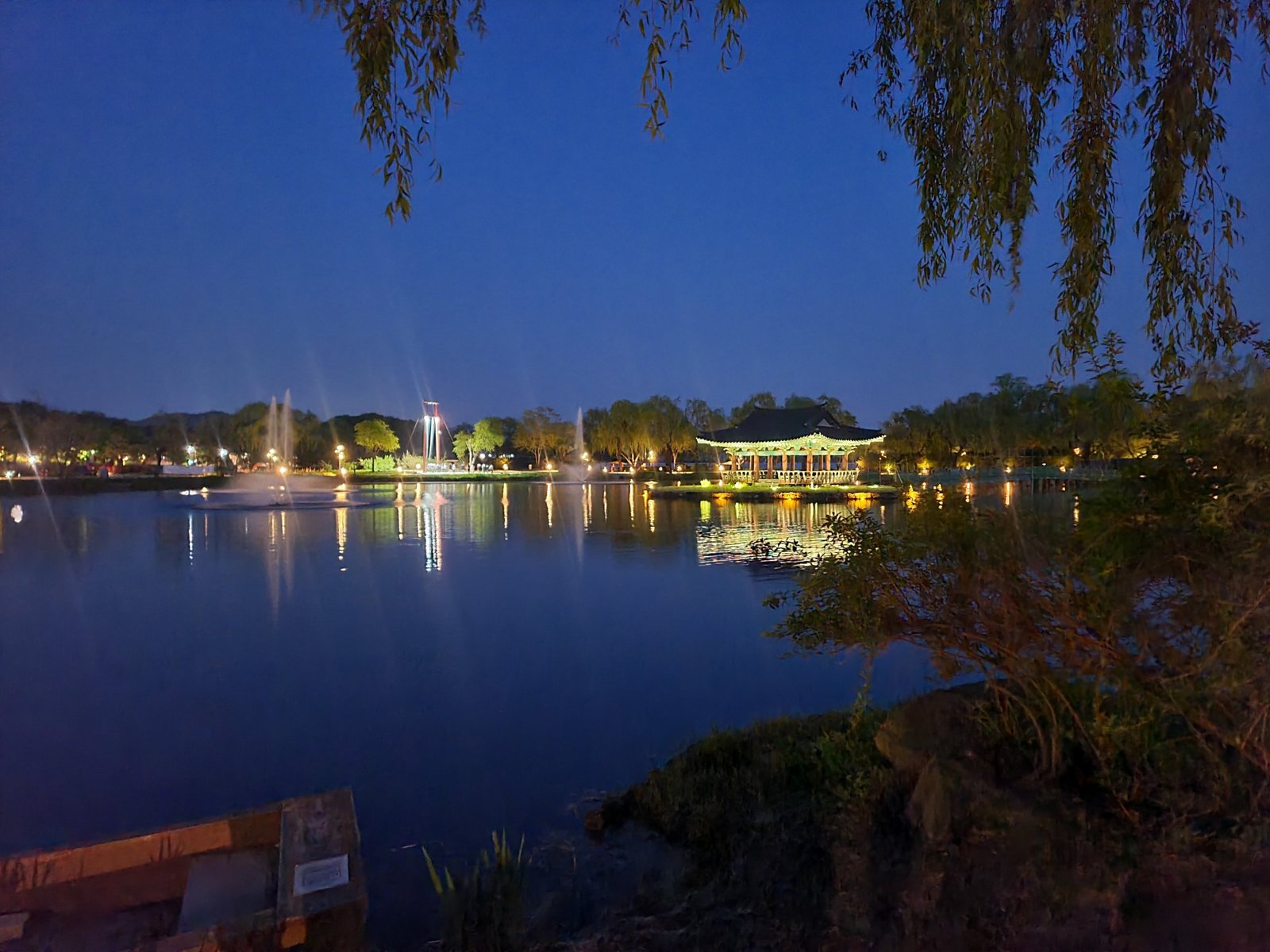 Poryongjeong pavilion lit up on Gungnamji pond at dusk, framed by willow branches